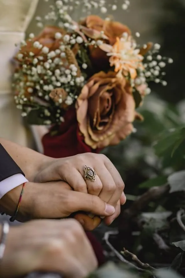 Deux personnes se donnent la main au premier plan avec un bouquet en arrière plan.